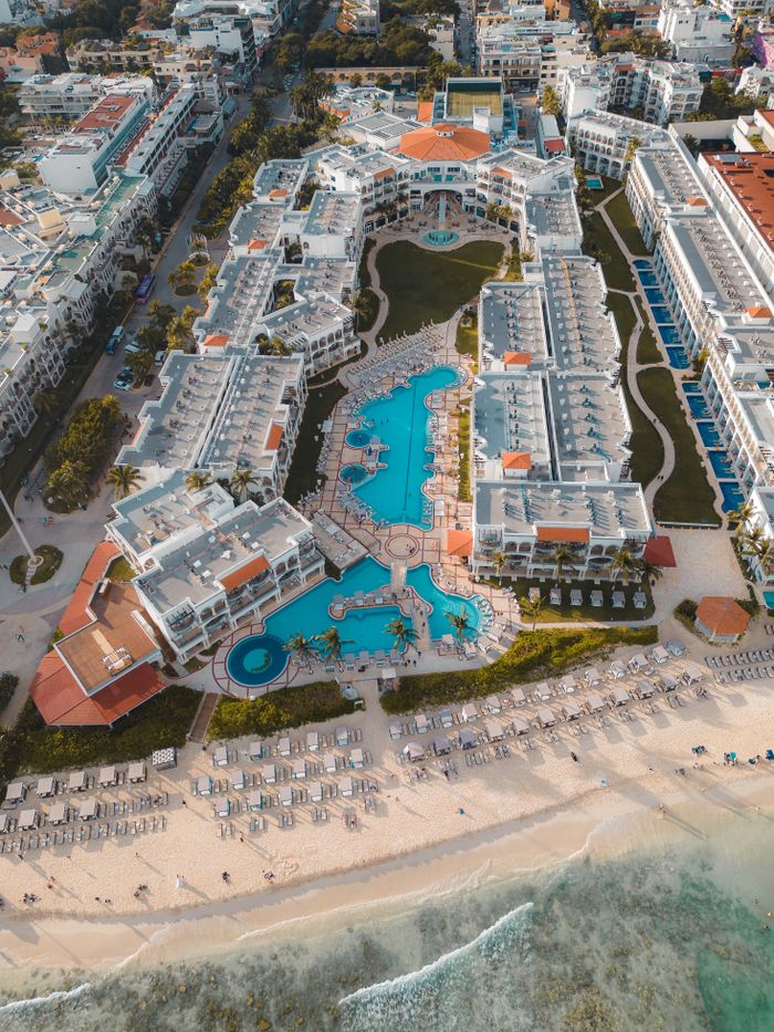 Aerial view of luxury beach resort in Playa del Carmen, showcasing pools and coastline.